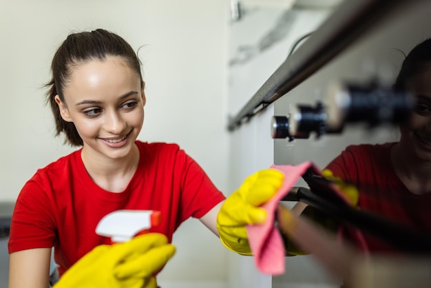 Free photo happy woman with bottle of spray cleanser cleaning oven at home kitchen