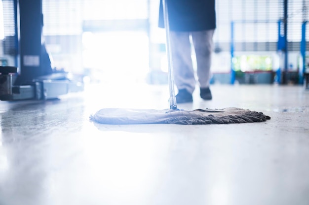 Photo mechanic in auto repair center cleaning using a mop squeeze water from the epoxy floor in the car repair service center