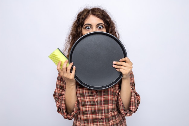 Free photo scared young cleaning woman holding sponge and covered face with tray isolated on white wall
