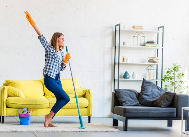 Free photo smiling young woman dancing in the living room with cleaning equipments