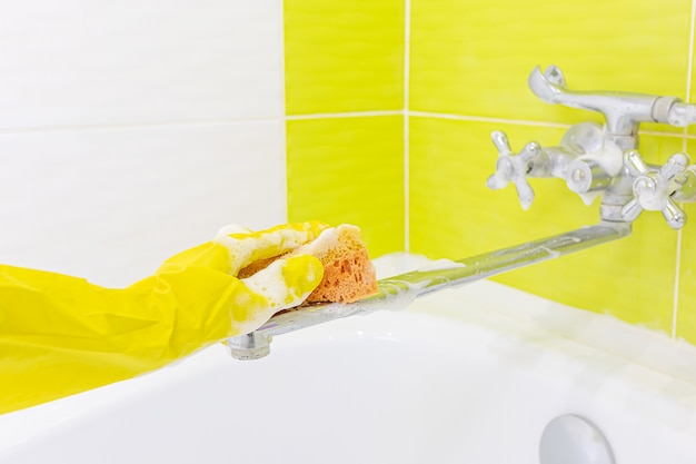 Uma mão feminina em uma luva de látex amarela esponja uma batedeira. Muita espuma. O conceito de limpar o banheiro, limpeza. Copyspace.