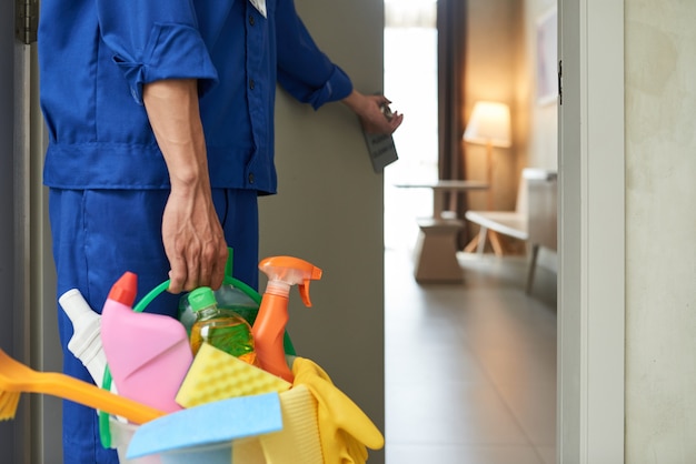 Free photo unrecognizable cleaner walking into hotel room with tools and detergents