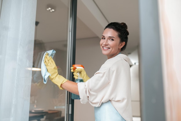 Free photo a woman in apron cleaning the windows and looking involved